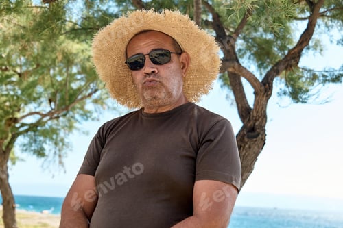 Preview: Overweight middle-aged smiling man wearing straw hat at seaside.