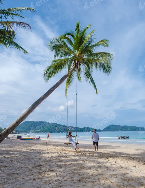 Preview: A couple of men and women on a swing under a palm tree at the beach of Patong Phuket Thailand