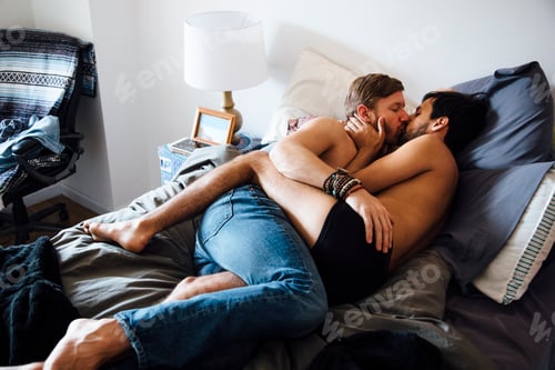 Preview: Male couple, partially dressed, lying on bed, kissing