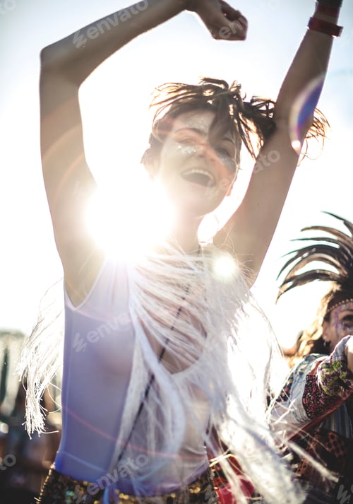 Preview: Young woman at a summer music festival arms raised, dancing among the crowd.