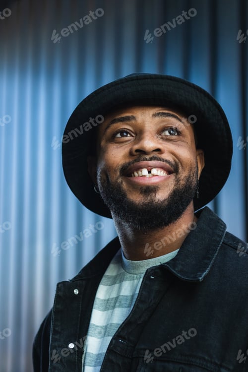 Preview: Smiling black hipster man in hat looking up