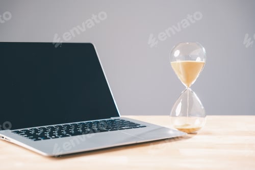 Preview: Time for business deadline, hourglass with sand flowing next to modern laptop computer,