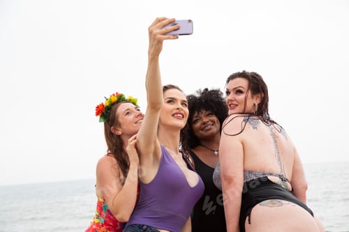 Preview: Mixed group of female friends having fun at the beach taking selfies.