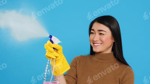 Preview: Housekeeper wearing yellow rubber gloves while holding spray and duster during houseclean