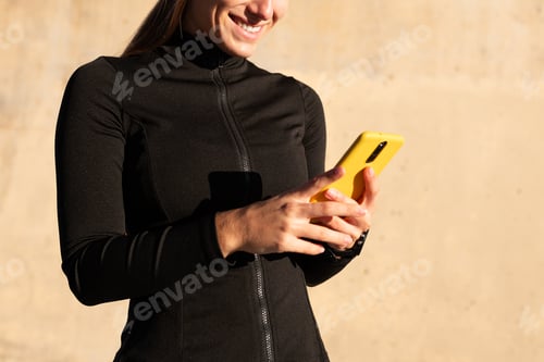 Preview: Smiling sportswoman using mobile phone after training outdoors