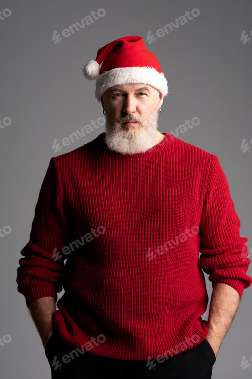 Preview: Stylish Santa. Middle aged man with beard wearing Christmas hat and red sweater looking at camera