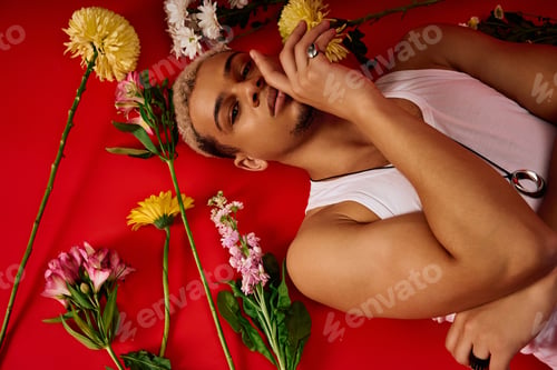 Preview: Young man showcases trendy fashion with vibrant floral arrangement in a red studio