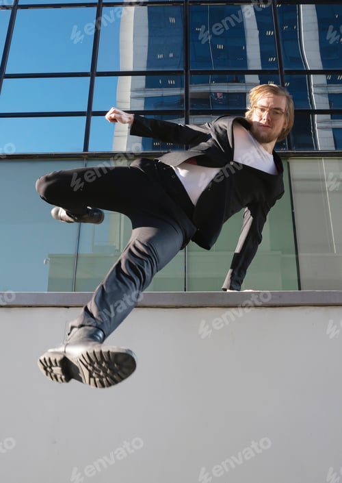 Vista previa: businessman jumping doing parkour with long blonde hair and glasses executive business clothes