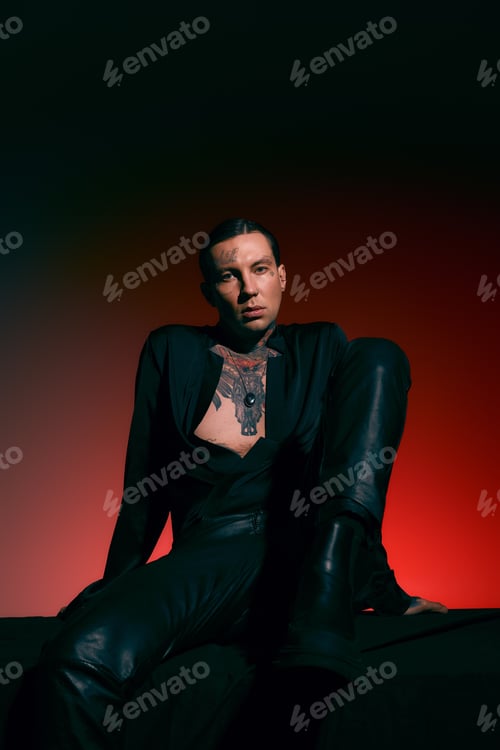 Preview: Stylish young man poses confidently in black attire with striking tattoos in vibrant lighting