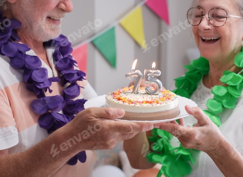 Preview: Senior couple laughing carefree celebrating a 75th birthday of husband holding a cake