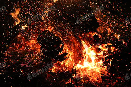 Preview: Burning red hot sparks rise from large fire at night.
