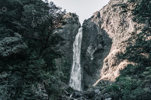 Preview: tall narrow waterfall with little water among the rocks of the mountains illuminated by sunlight