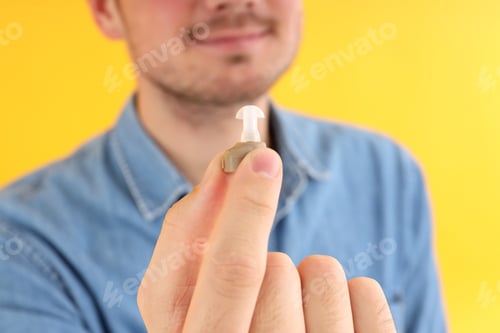 Preview: Young man hold hearing aid on yellow background