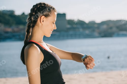 Preview: smiling sportswoman looking at smart watch on beach