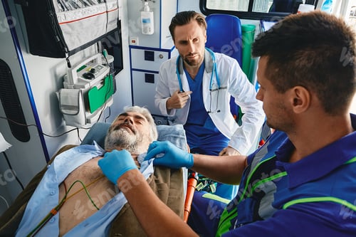 Preview: Cardiac patient in ambulance. Paramedics performing ECG on male vicitm lying on stretcher with