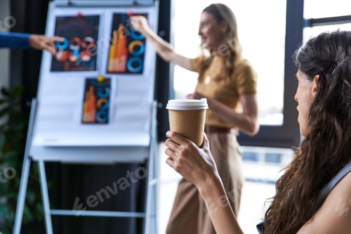 Preview: businesswoman with coffee to go looking at colleagues talking near flip chart with graphs in office
