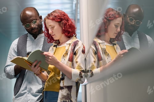 Preview: Two young intercultural employees or students looking through notes in copybook