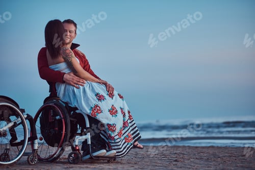 Preview: Woman sits on her husband's lap, resting on a beach against a background of a bright dawn.