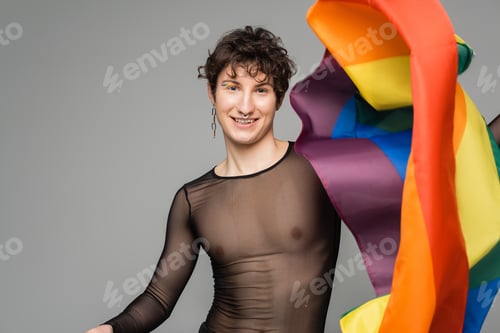 Preview: cheerful nonbinary person in black transparent top and silver accessories holding lgbt flag isolated