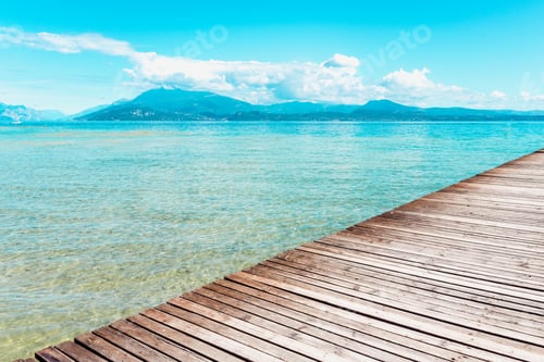 Preview: Planked wooden walkway over a tranquil lake with high mountains in the background