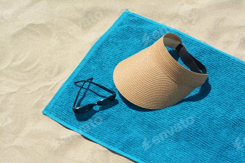 Preview: Towel, straw visor cap and sunglasses on sand. Beach accessories