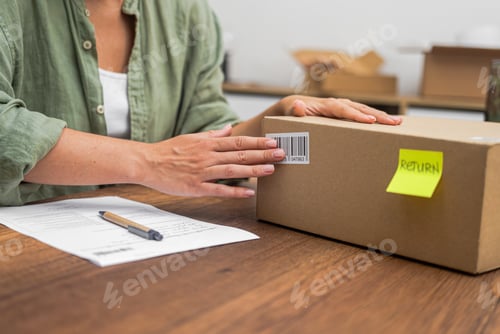 Preview: Hands of female consumer stick barcode on cardboard box with yellow sticker with word Return