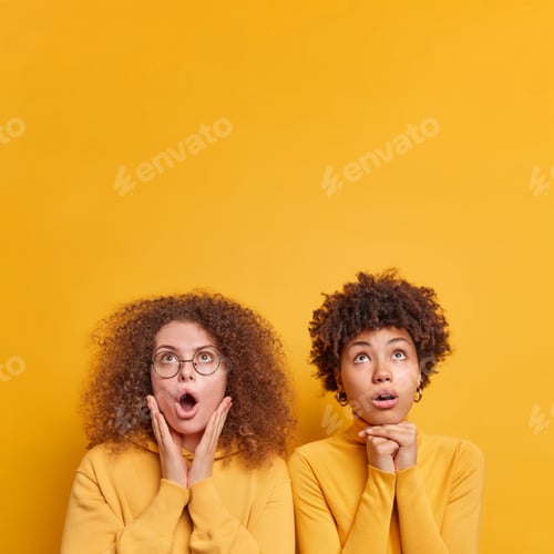 Preview: Vertical shot of two diverse women stare with shock above keeps mouth opened stand closely to each o