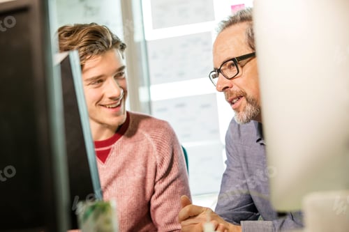 Preview: Male digital designer explaining design to trainee at office desk