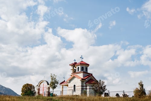 Preview: White brick church with a red roof in a field with a metal fence