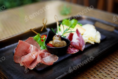 Preview: Sliced meat and cheese appetizer with pickled olives and lettuce leaves. Cold appetizers