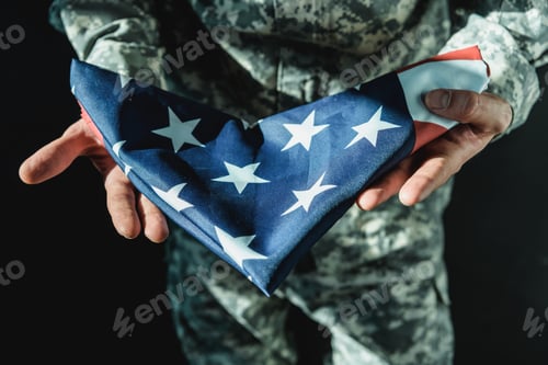Preview: cropped shot of soldier holding folded united states flag isolated on black