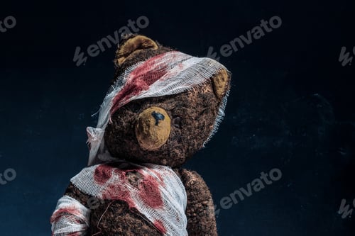 Preview: Old brown teddy bear wrapped in bloody bandages on a black background