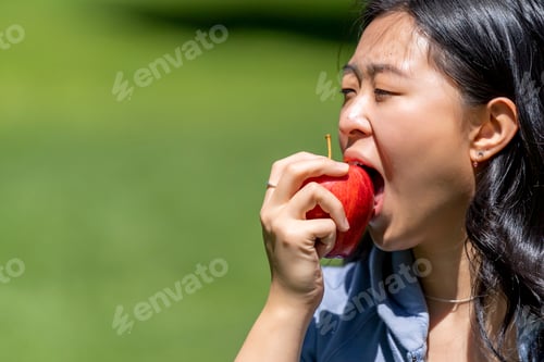 Preview: Asian woman biting a red apple in the park