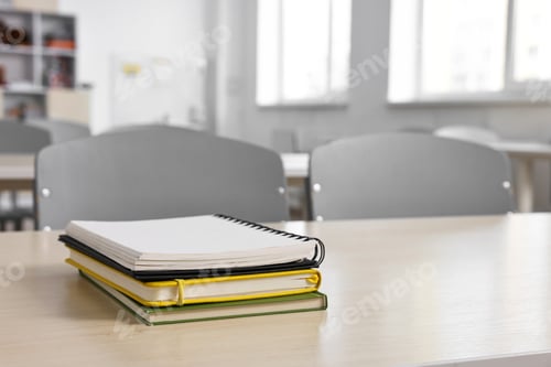 Preview: Stack of notebooks on wooden desk in empty classroom