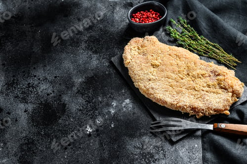 Preview: Raw Wiener Schnitzel, breaded steak ready to cook. Black background. Top view. Copy space