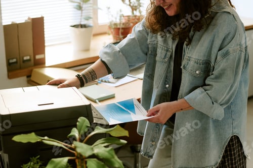 Preview: Young Adult Caucasian Woman Smiling While Printing Documents in Office Setting