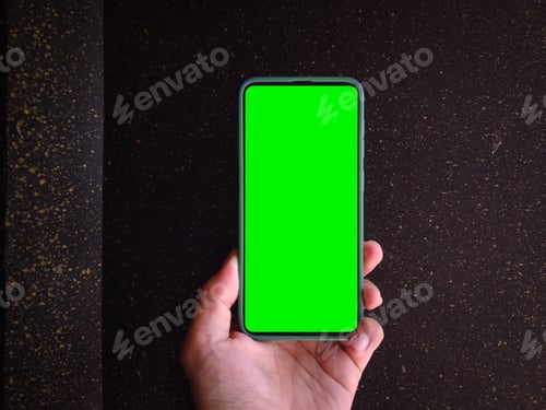 Preview: Man hand hold smartphone with green screen on dark room