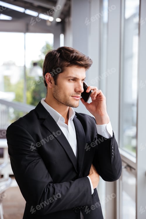 Preview: Serious young businessman talking on cell phone in office