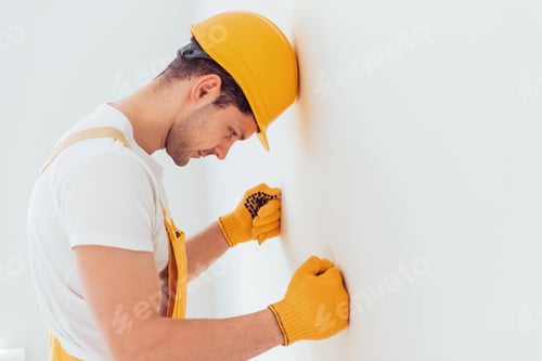 Preview: Depressed handyman in yellow uniform stands against wall. House renovation conception