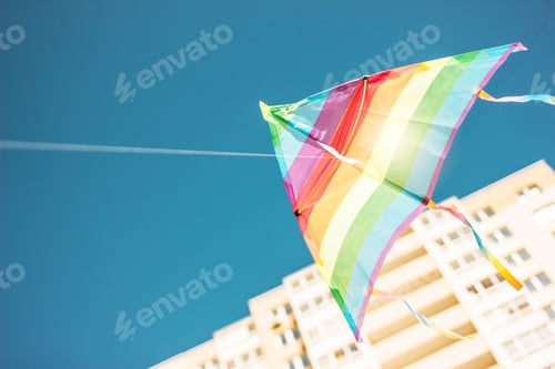 Preview: Rainbow colored kite flying in blue sky in city. Freedom and summer holiday