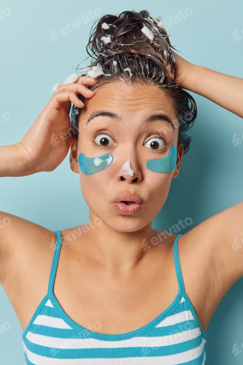 Preview: Shocked woman washes hair and applies hydrogel patches to reduce fine lines stares at camera with om
