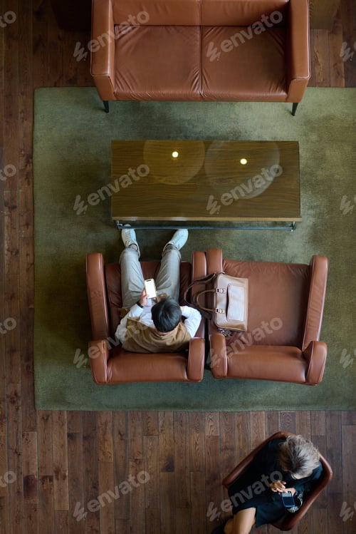 Preview: Above view of two young business people texting in mobile phones in lounge