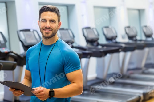 Preview: Male gym instructor standing in gym by treadmills holding clipboard wearing smartwatch and whistle
