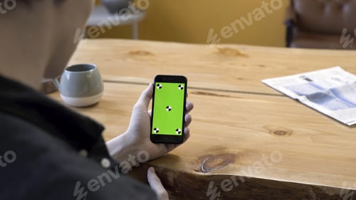Preview: View over the shoulder of a businessman using the hand held cellphone with green screen touchpad on