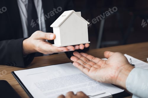 Preview: Real estate agent congratulations to new buyer by giving house model to client in the agency office.