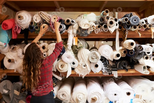Preview: Young woman reaching to select fabric from storage shelves