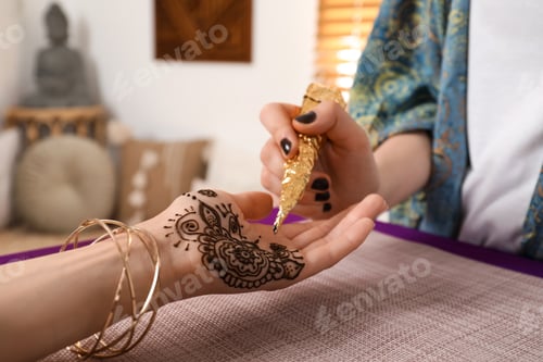 Preview: Professional mehndi master making henna tattoo indoors, closeup