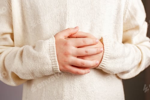 Preview: Close-up of a child's hands folded on the stomach in a light knitted champagne-colored sweater.