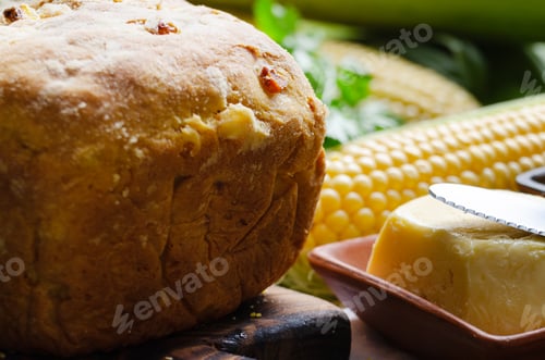 Preview: Zoomed view at homemade loaf of cornbread on wooden kitchen table. Cobs and butte aside