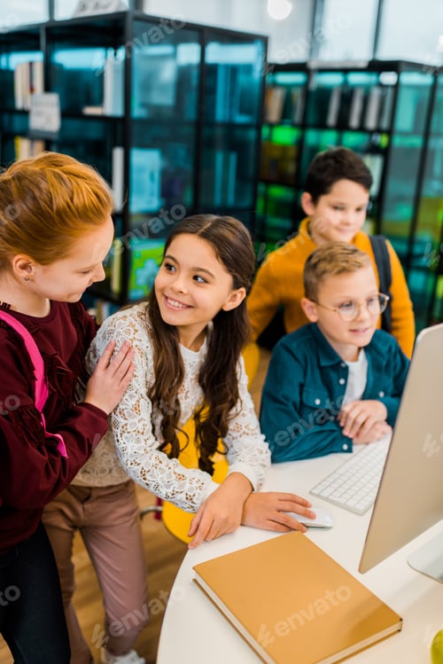 Preview: beautiful happy schoolchildren using desktop computer together in library